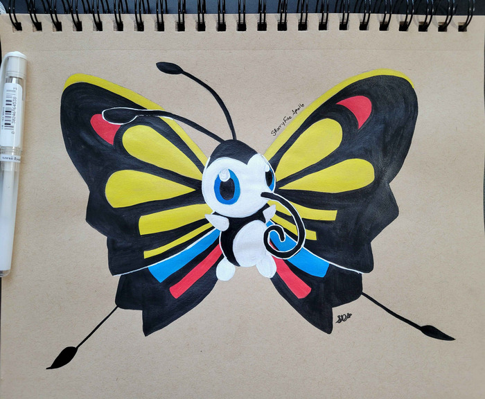 Colorful Beautifly painted in bold black India ink with yellow, red, blue, and white wing markings on a tan spiral sketchbook